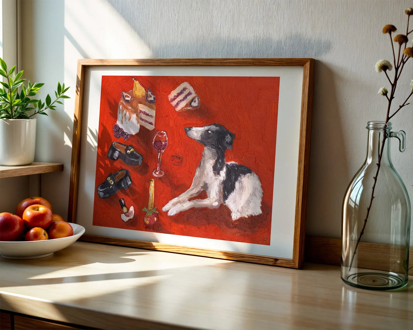 A Girl and Her Dog no. 1 by Leah Boyd is a limited edition art print featuring a black and white dog, cake, wine, and more on a red background, displayed on a sunlit kitchen counter with a plant, peaches, and glass bottle nearby.