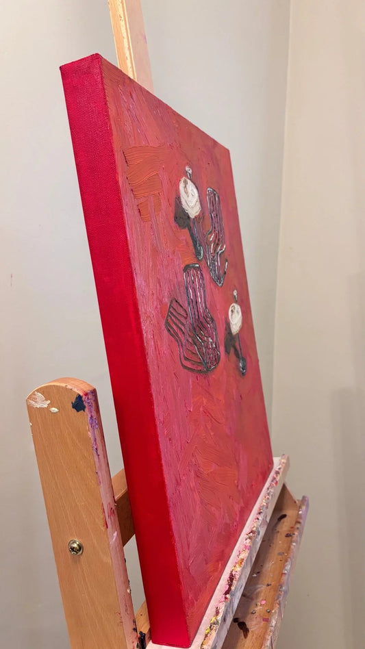Croissants & Espresso Martinis" by Leah Boyd is a textured red oil painting on an easel, featuring abstract forms and painted canvas edges. Displayed against a light wall, it's perfect modern art for your space.