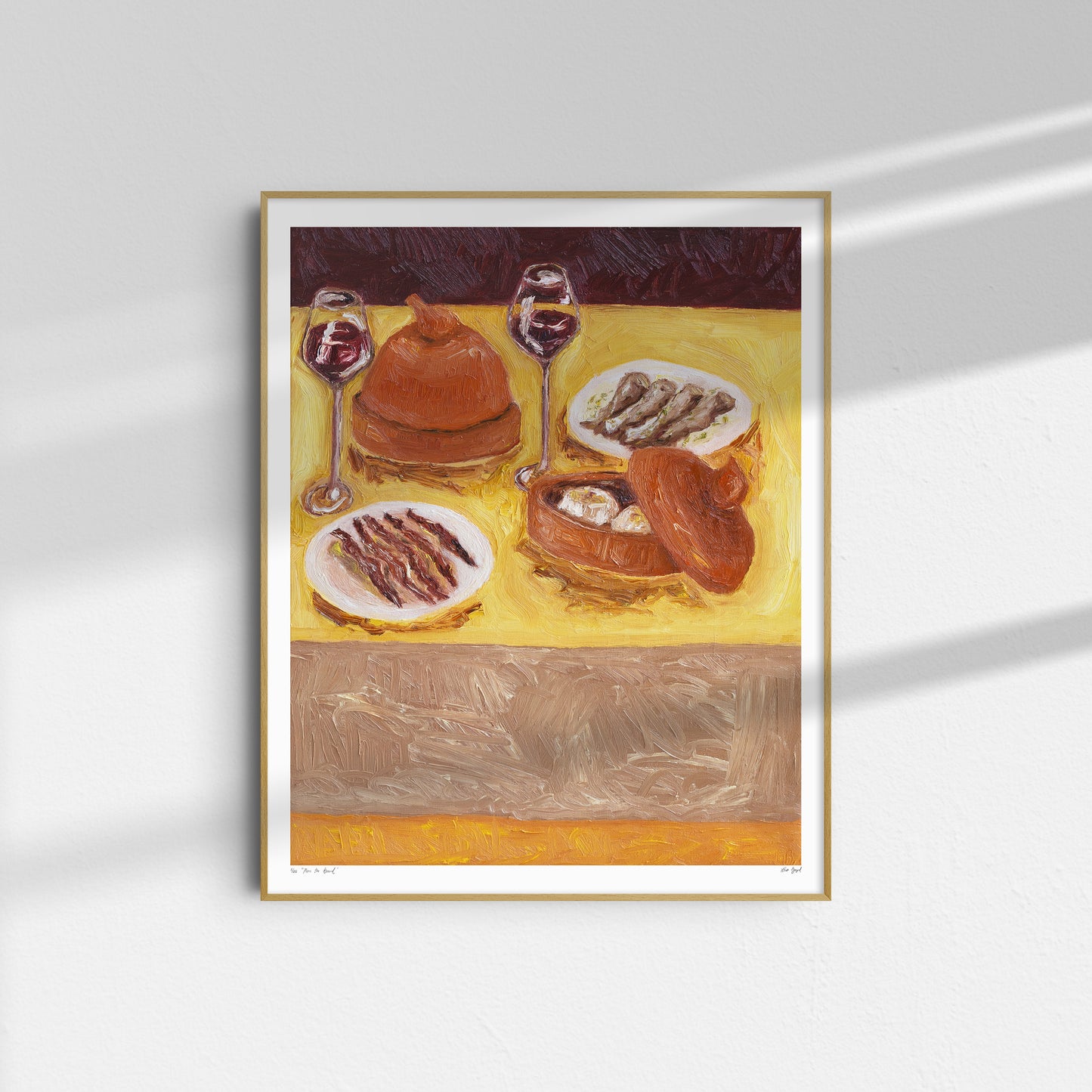 Pass the Bread" by Leah Boyd is a framed oil on canvas painting featuring a table set with bread, fish, and two glasses of red wine on a yellow tablecloth, displayed on a white wall with sunlight creating gentle shadows.