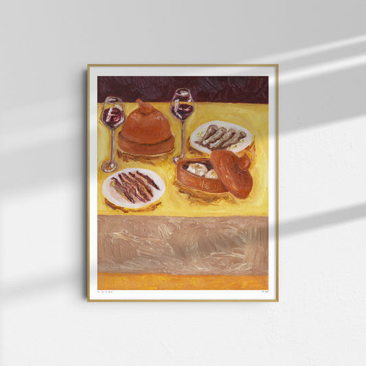 Pass the Bread" by Leah Boyd is a framed oil on canvas painting featuring a table set with bread, fish, and two glasses of red wine on a yellow tablecloth, displayed on a white wall with sunlight creating gentle shadows.