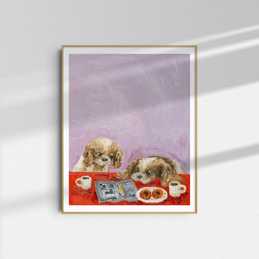 A framed limited edition art print titled “Cavalier Conundrum” by Leah Boyd, depicting two dogs sitting at a table with coffee cups, a newspaper, and pastries against a light purple background, hangs on a white wall.
