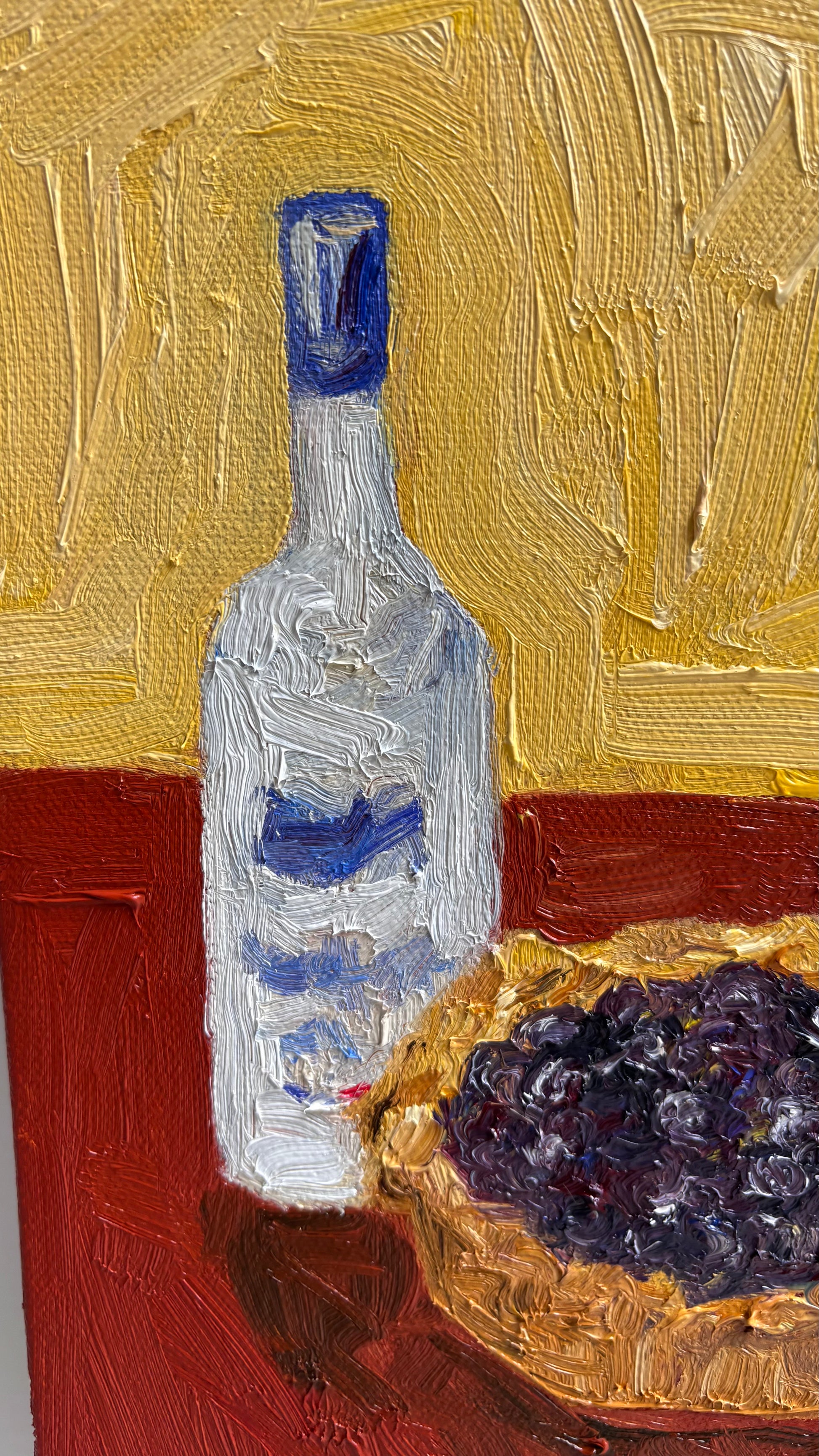 Leah Boyd’s “The Key to Pie Crust is Vodka” is an original oil painting featuring a clear bottle with a blue label next to a bowl of dark purple grapes on a vivid red and yellow textured background.