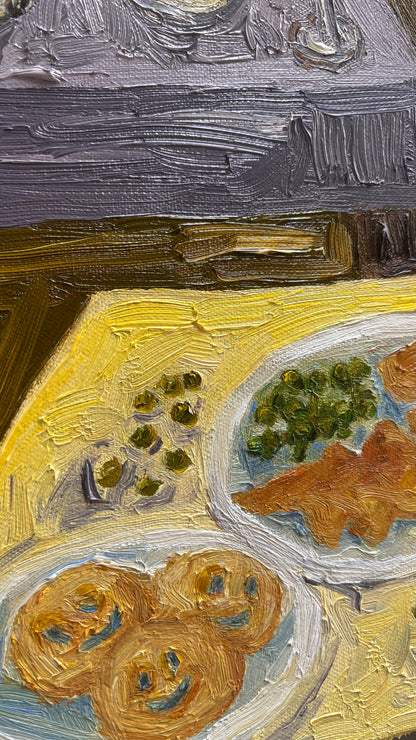 A close-up of "The Kids Table" by Leah Boyd, an impressionist original oil painting on canvas depicting plates of food with pretzel shapes and green vegetables on a yellow tablecloth. Features bold texture and includes certificate of authenticity.