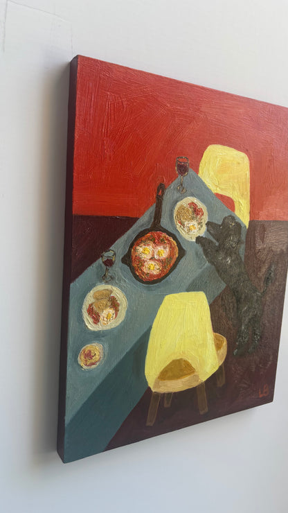 Dinner for One no. 5: Shakshuka by Leah Boyd is a vibrant oil painting on cradled wood panel featuring bold reds, blues, and yellows, a set table with food and wine, two yellow chairs, and a black cat reaching for a plate.