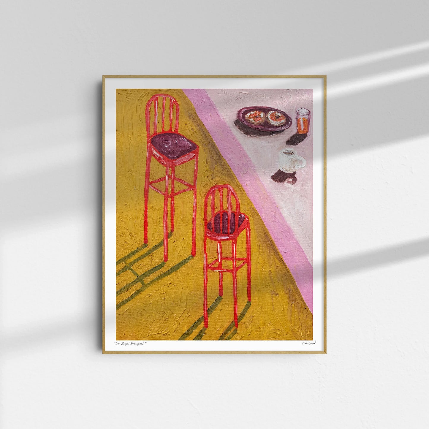 The "Lox Bagel Breakfast" framed print by Leah Boyd shows two red bar stools casting long shadows on a yellow floor, with a countertop of plates, coffee cups, and juice in a textured, impressionistic style.