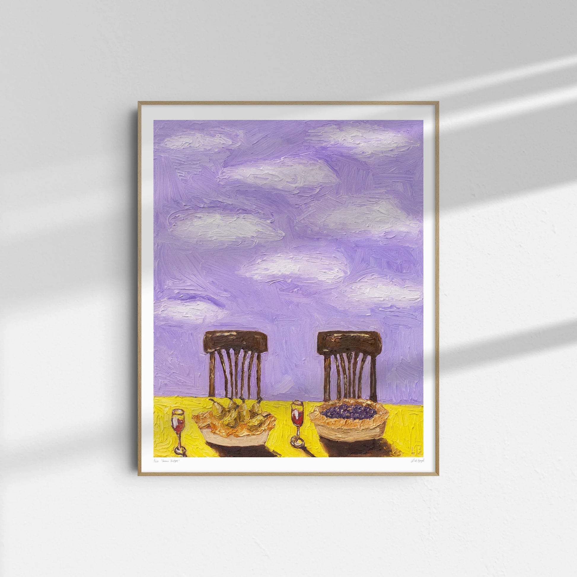 "Summer Twilight" by Leah Boyd is a framed limited edition art print featuring two empty chairs at a chartreuse table with wine and fruit pie under a lavender sky with white clouds. Delicate shadows fall across a white wall.