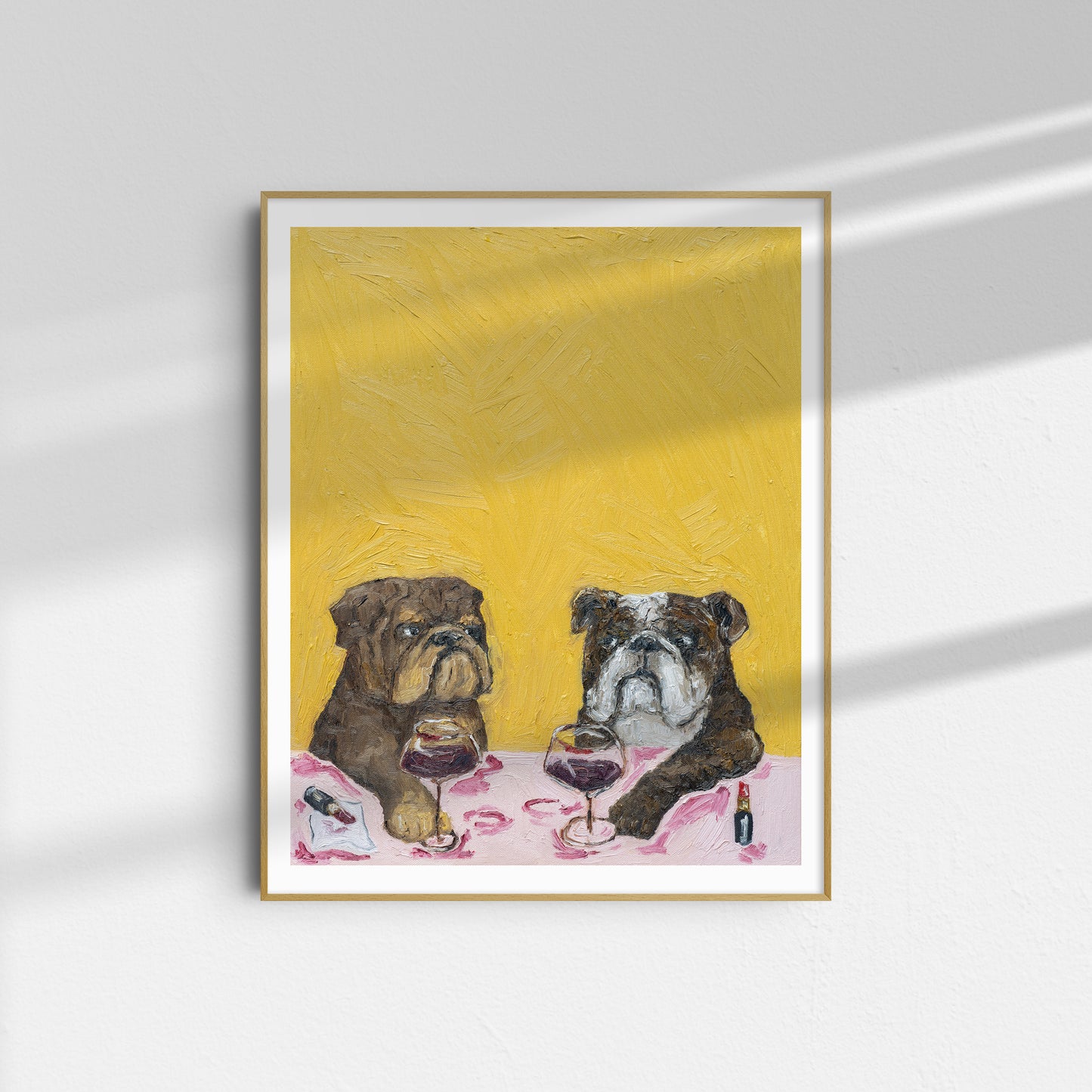 Introducing “Wine Night & Gossip” by Leah Boyd—a limited edition framed art print featuring two bulldogs seated at a table with wine glasses and bottles, set against a textured yellow background, exquisitely reproduced from the original oil on canvas.