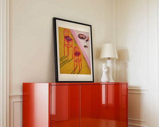 A modern room with a Lox Bagel Breakfast by Leah Boyd, a white sculptural lamp, and a glossy red cabinet, all set against cream-colored walls.